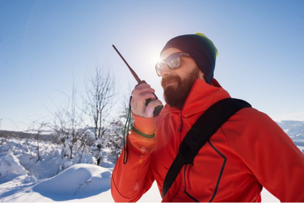 A mountain climber dressed in a red winter coat and a black winter hat is calling his colleague who is found at a higher point of the mountain to coordinate his scale up the mountain; it is winter time. With tech support outsourcing solutions, mountain climbers - such as this - are ensured to have non-stop service that gives them continual peace of mind - without limitations.